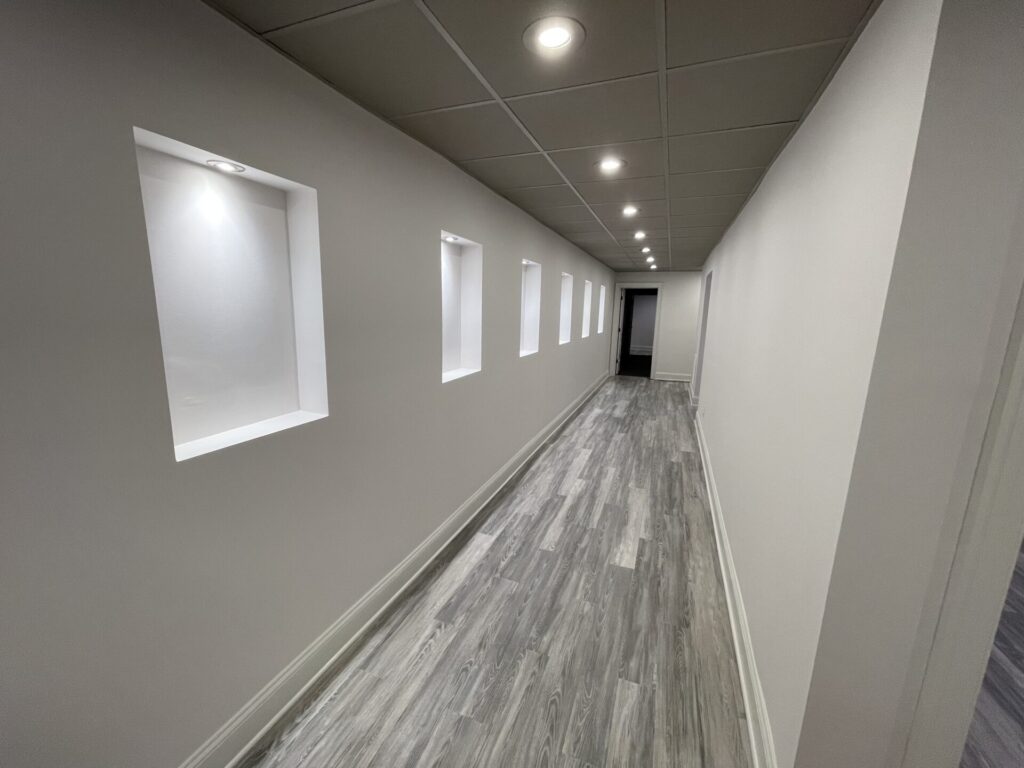 Hallway with grey LVP flooring, recessed LED lighting, and lighted niches